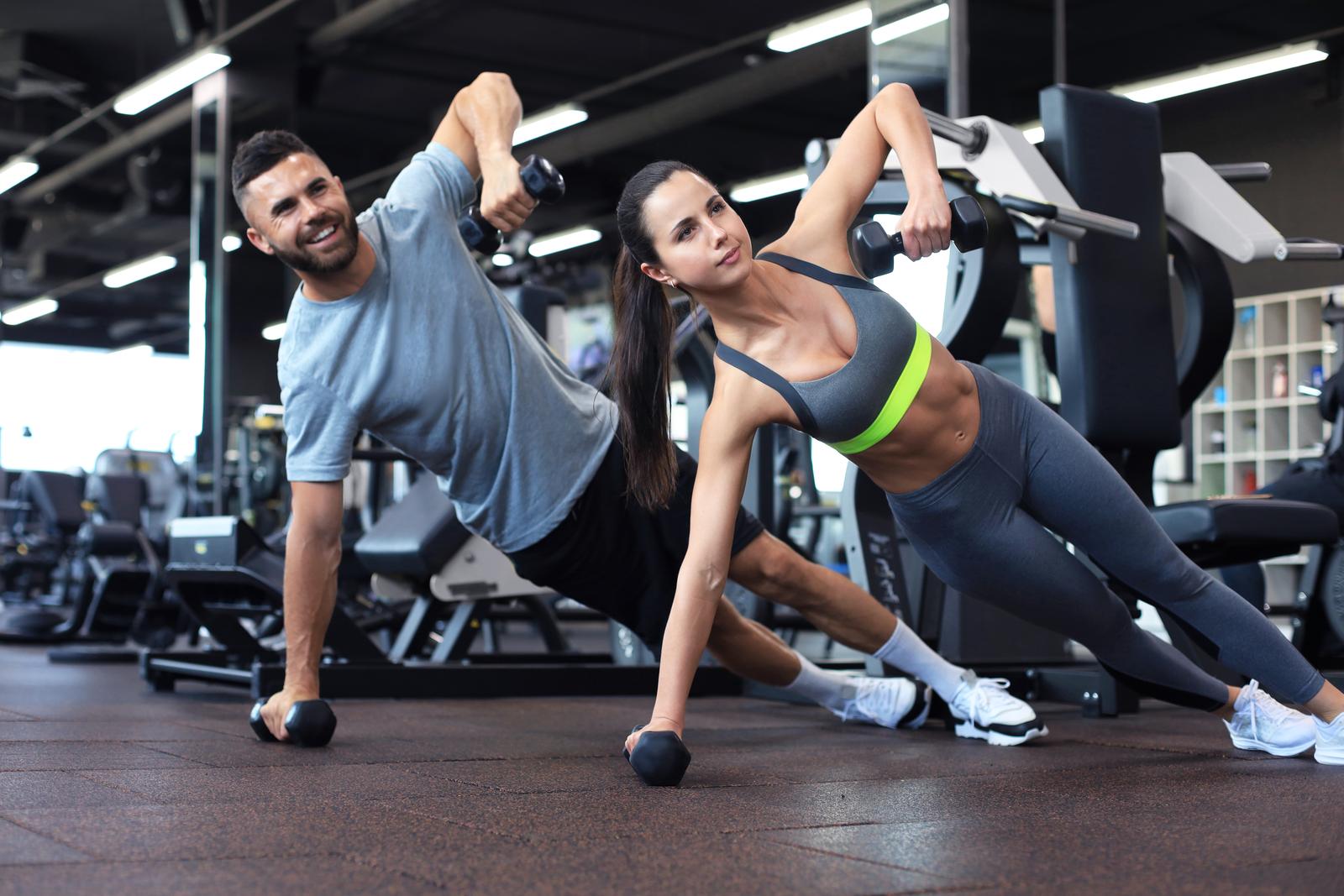 Strong man and woman holding dumbbells in plank position at the gym